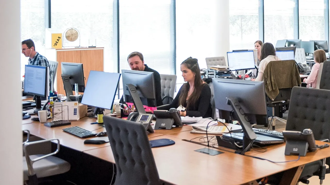 A busy open-plan office, staff working at desks with phones.