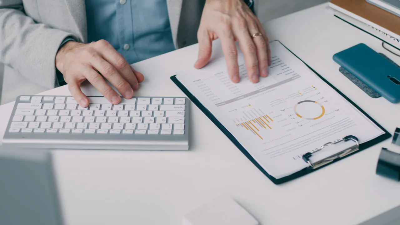 An accountant working at a keyboard beside a printed financial report.