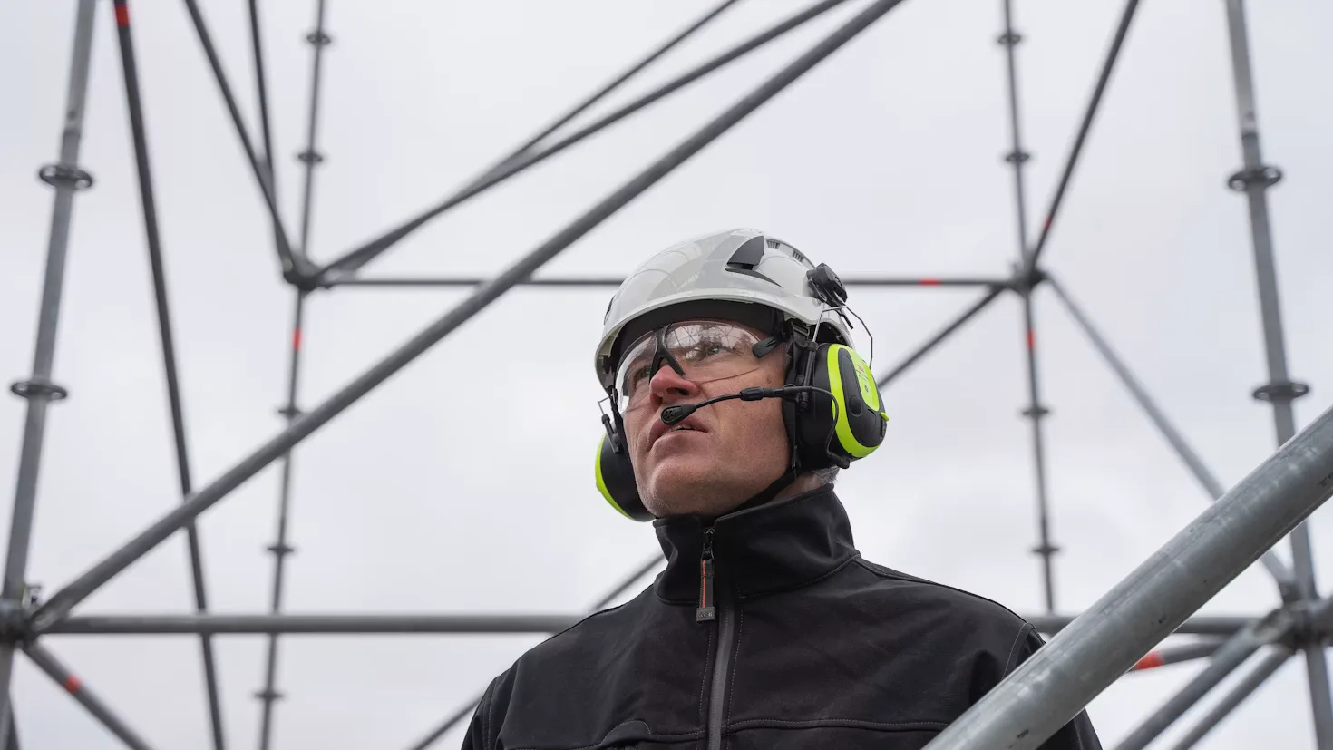 A construction worker in a hard hat and headset on a call at a scaffold.