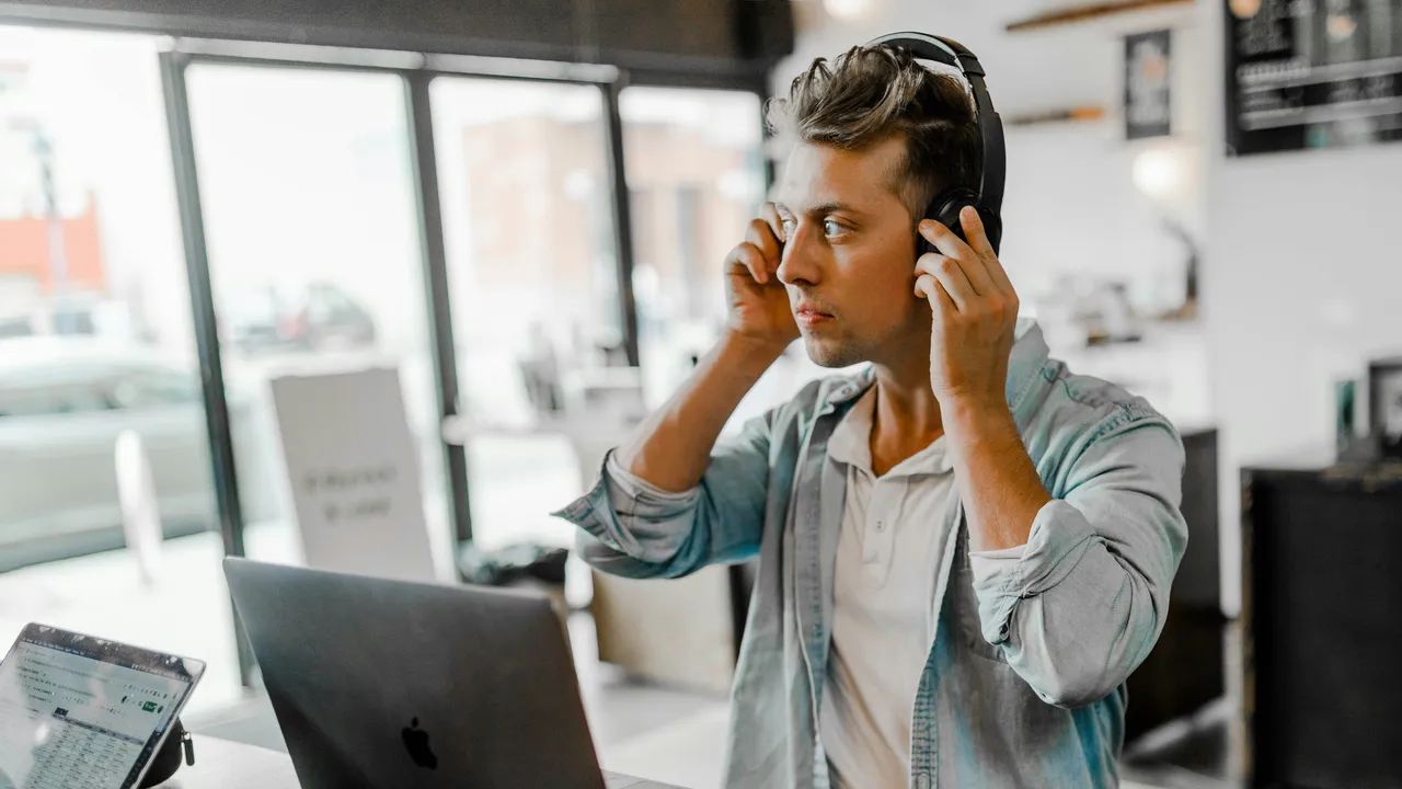 A person taking a business call on a headset at a home desk with a laptop.
