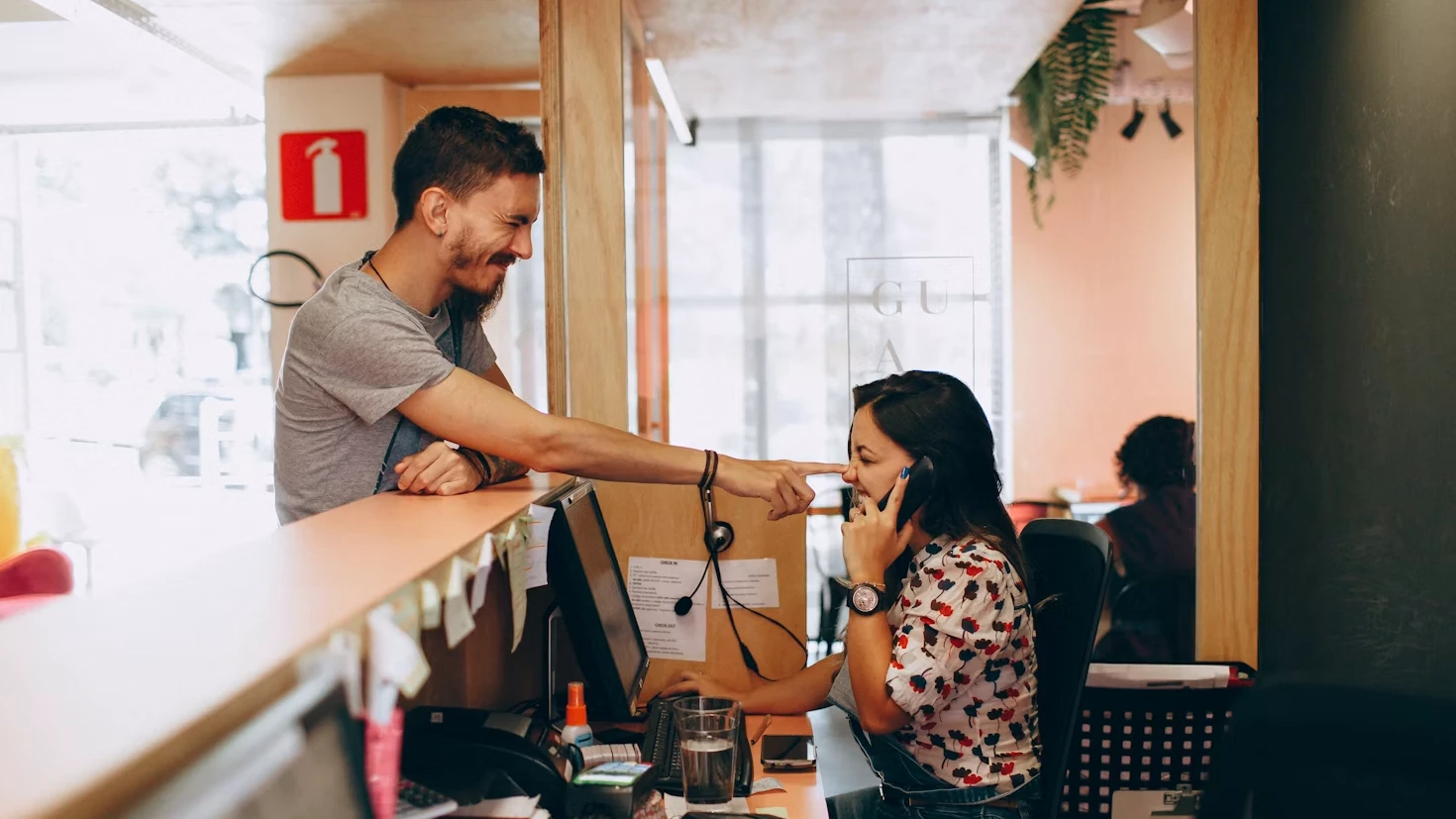 A hotel receptionist taking a call at the front desk while a guest checks in.