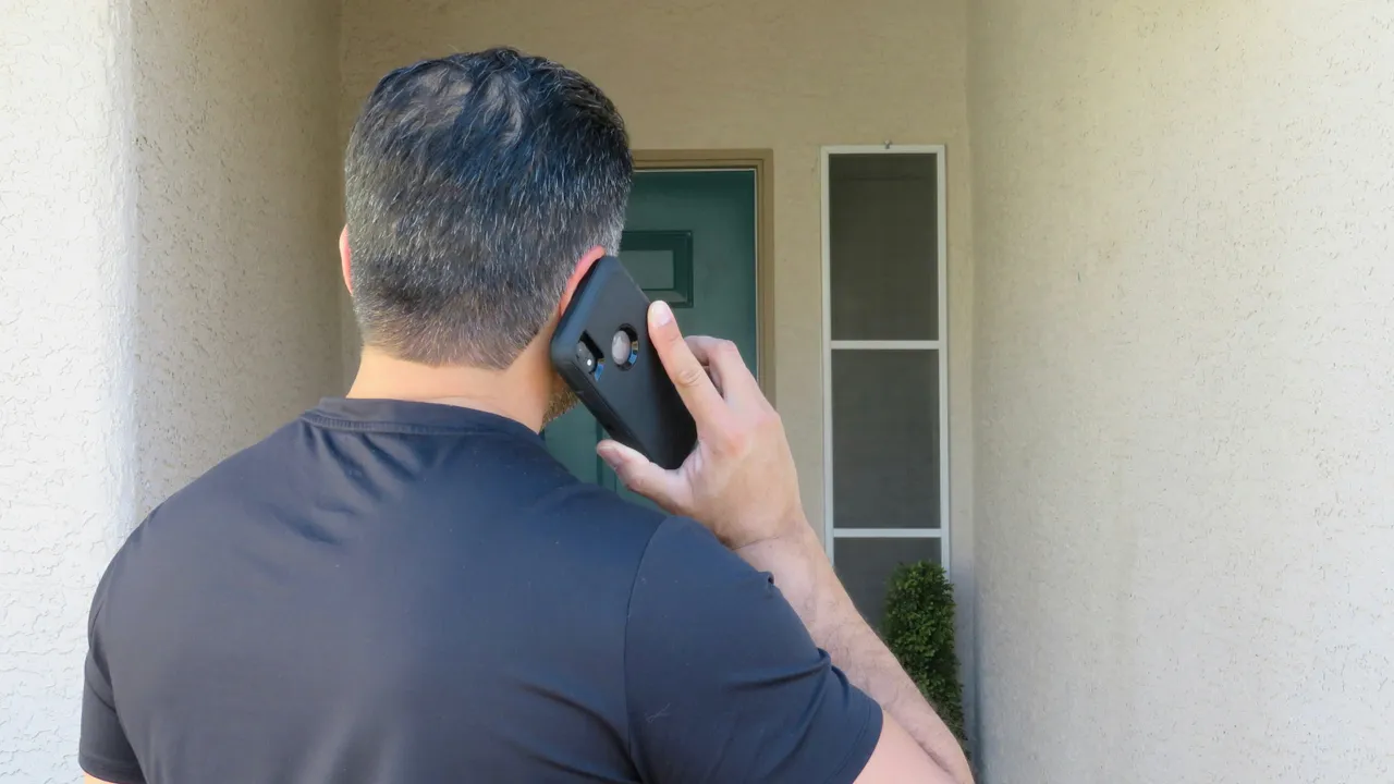 An estate agent taking a call on a phone outside a house.