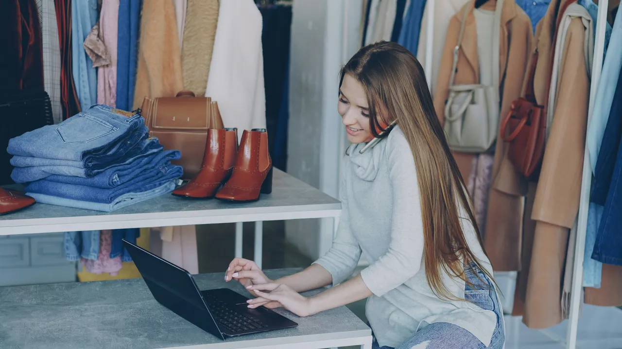 A shop owner on the phone at the counter of a clothing boutique.
